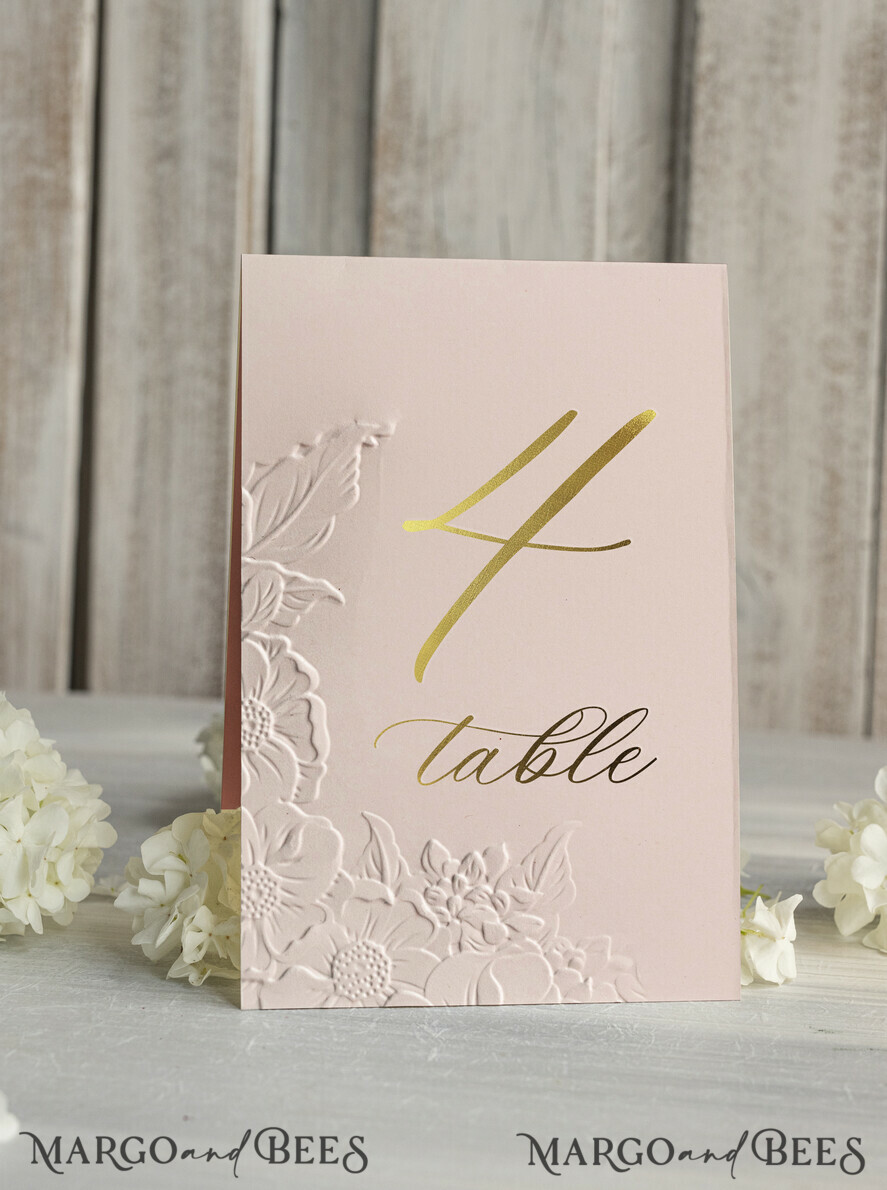 TISCHDEKORATIONSCHILDER   Glitzer Elegante goldene Hochzeitstischnummernkarten mit geprägtem Blumendesign, roséfarbenem strukturiertem Papier, gefaltetem Zeltstil, klassischer Schriftart, luxuriöser Empfangsdekoration.